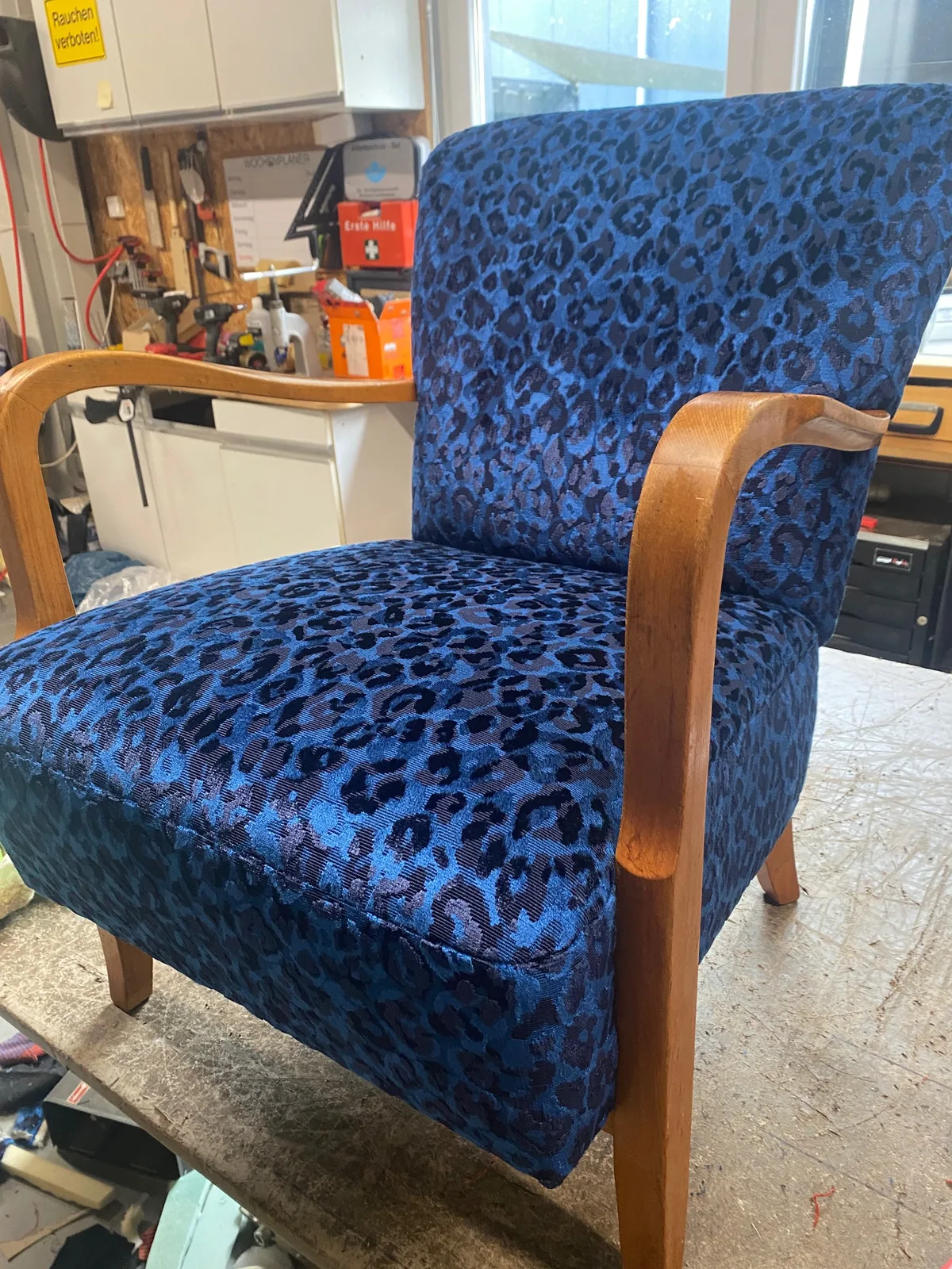 Fertig bezogener Sessel mit blauem Musterstoff und geschwungenen Holzarmlehnen